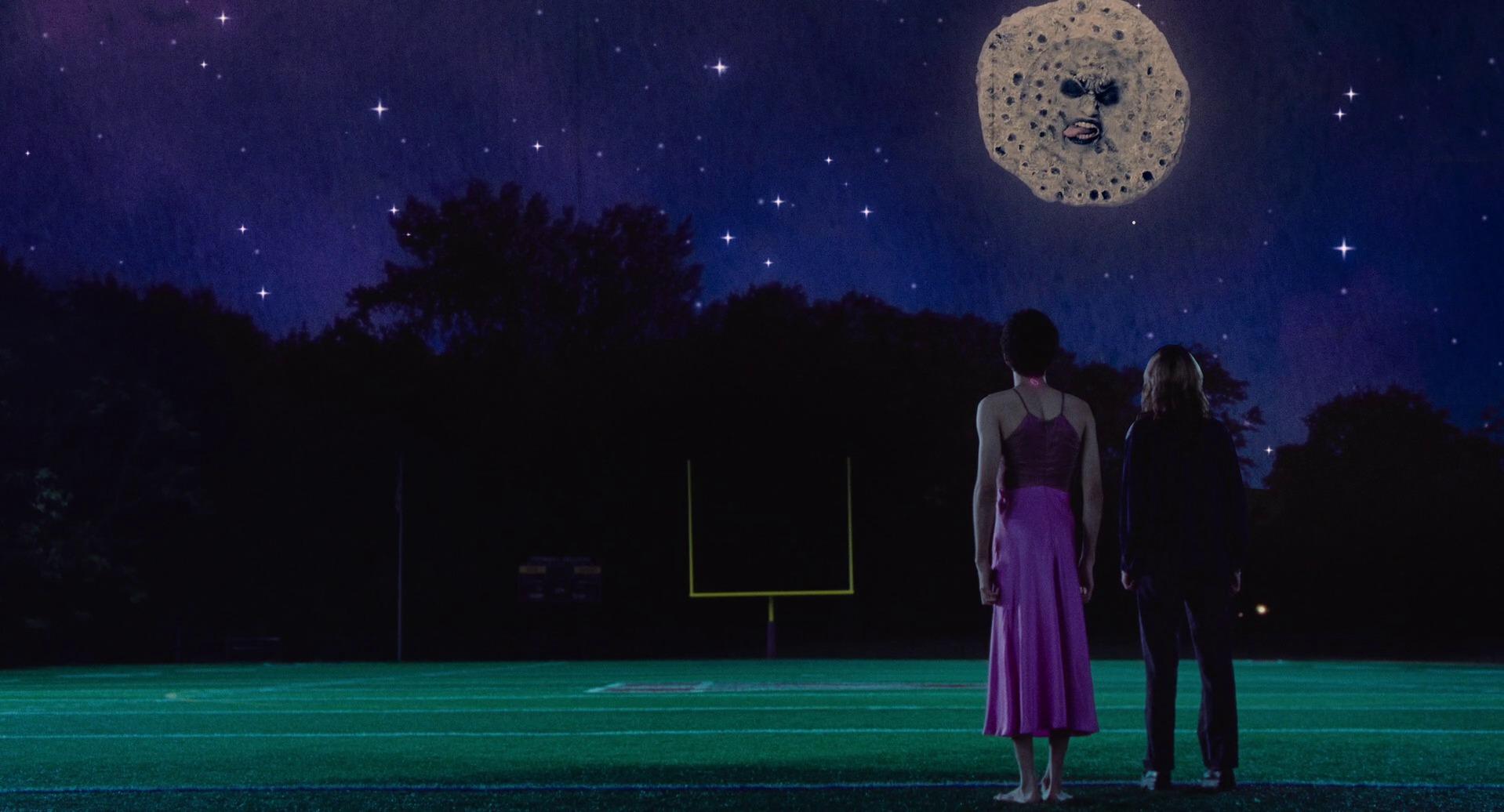 Maddy with Owen in a dress, facing away from the camera, and Mr. Melancholy in the sky