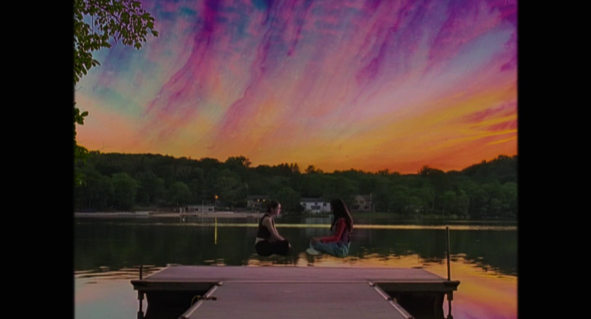 Tara and Isabel sitting on a dock under a sunset